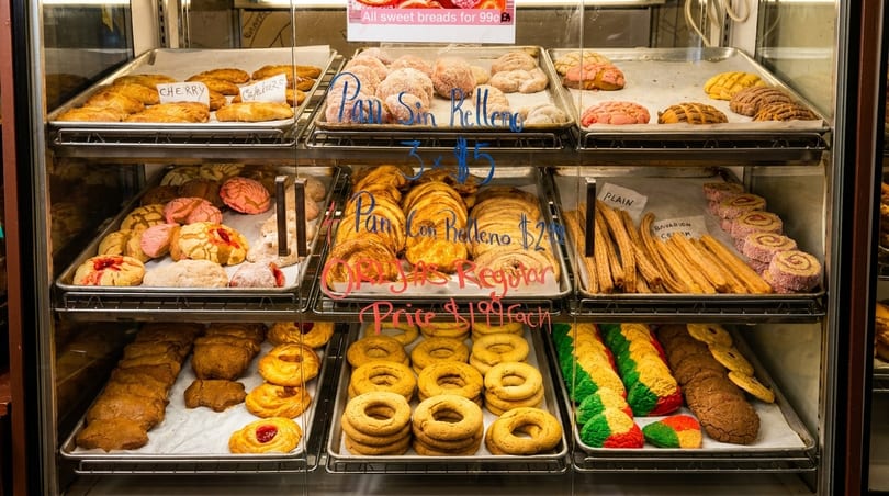 A bakery display case filled with various Mexican pastries, including conchas, churros, and empanadas.