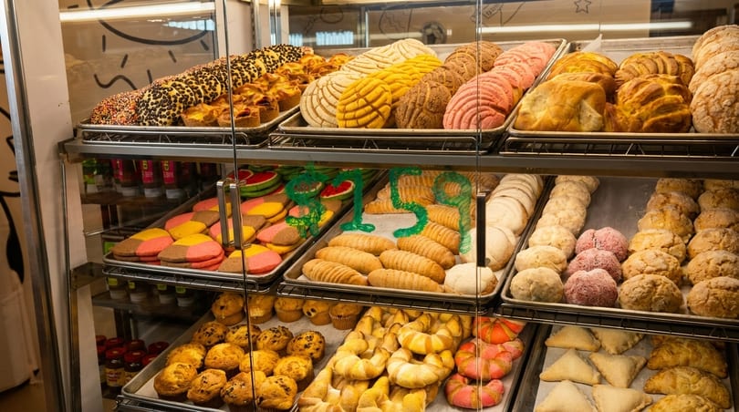 A glass display case filled with various colorful Mexican pastries, cookies, and muffins.