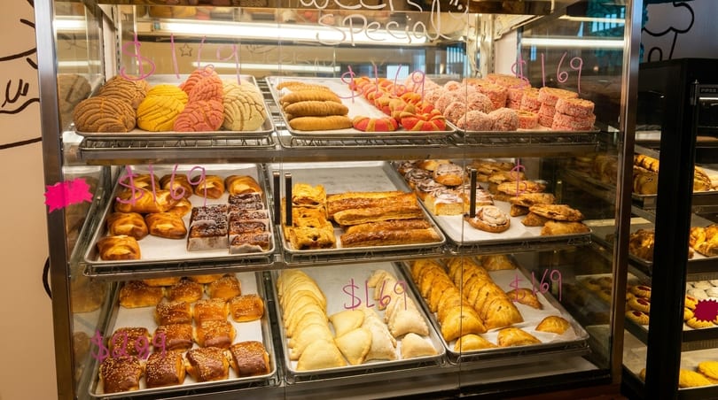 A brightly lit bakery display case filled with various pastries, breads, and sweet treats.